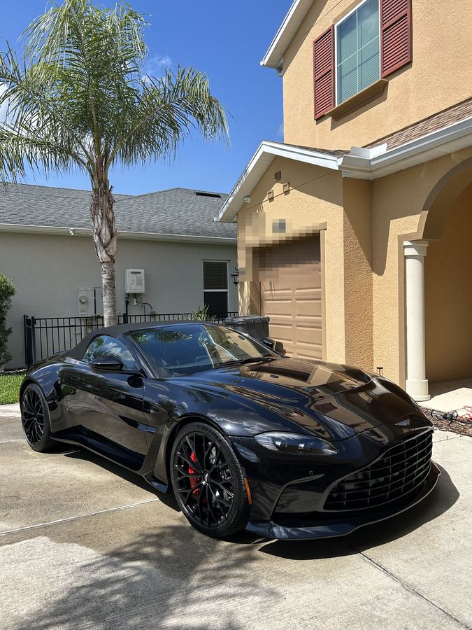 Black Aston Martin Vantage Roadster on a driveway, the paint holding a hard, wet-looking gloss