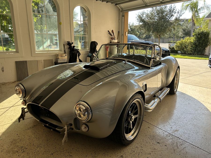 Silver Shelby Cobra 427 replica with black stripes, detailed in an open garage