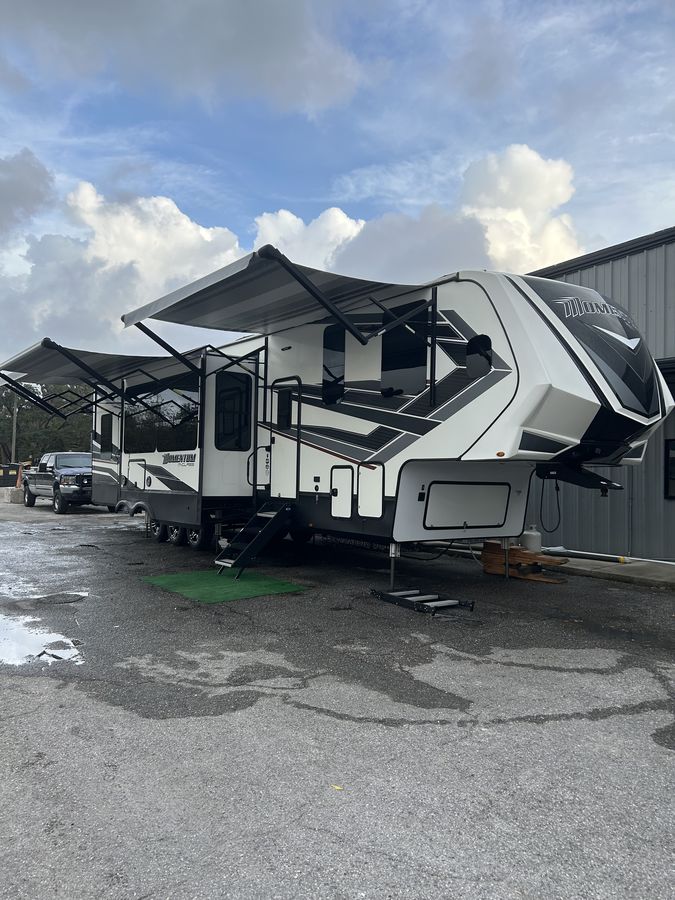 A large fifth-wheel RV washed down under its awning at a storage lot