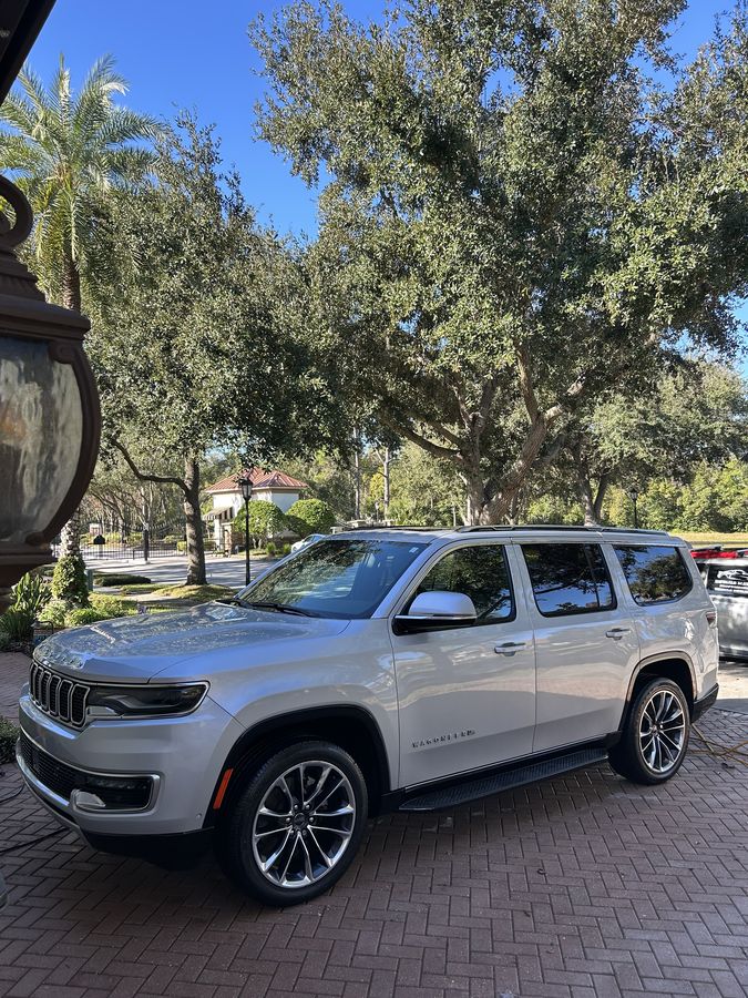 Silver Jeep Grand Wagoneer on block paving under heavy tree cover