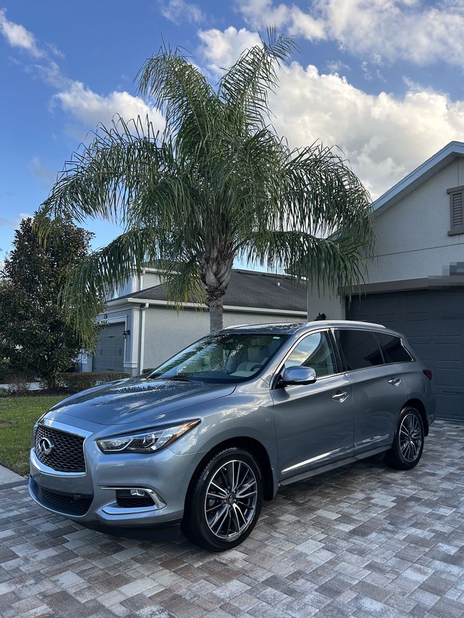 Silver Infiniti QX60 on block paving under a palm