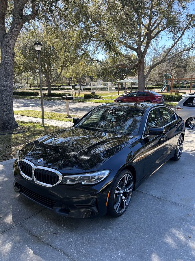Black BMW 3 Series with the bonnet reflecting the trees above it