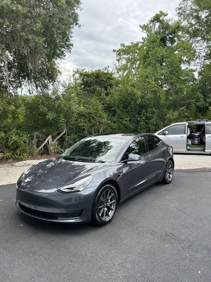 Grey Tesla Model 3, finished, with the van still parked behind